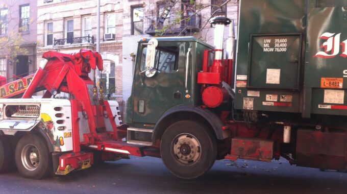 A Garbage Truck Being Towed On The Streets Of A City